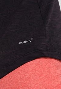 Musta urheilu kangas, jossa on teksturoitu pinta, ja valkoinen "drytivity" -logo. Yllä on kiinteä korallinvärinen tekstiili.