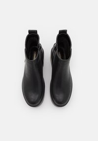 Par de botas de cuero negro hasta el tobillo con cremalleras laterales y lengüetas de tirón, vistas desde arriba sobre un fondo blanco liso.