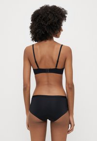 Svart bikinisett med et enkelt design, tynne regulerbare stropper og lavtsittende shorts. Glatt tekstur uten mønstre eller pynt.