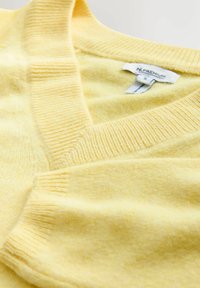 Gul strikket sweater med V-udskæring, der har ribkant ved ærmer og hals. Blødt materiale, enkelt design og en simpel etiket indeni.