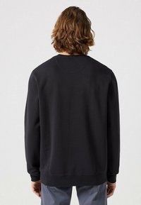Felpa nera a girocollo con maniche lunghe, texture liscia e polsini e bordo a costine. La vista posteriore mostra un design semplice senza decorazioni.