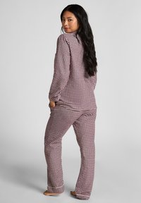 Czerwono-białe w kratkę piżama składająca się z długich rękawów i luźnego kroju. Miękka tkanina z kołnierzykiem i kieszeniami. Spodnie mają prostą nogawkę.