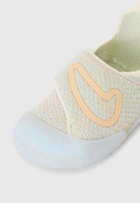Jemne textúrovaná pastelová obuv na slip-on s béžovým akcentom a transparentnou gumovou podrážkou, so hladkým detailom loga na boku.