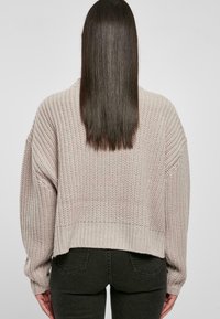 Pull court effet grosse maille de couleur beige clair avec un motif texturé. Comprend un ourlet côtelé et des manches oversize, associé à un jean foncé.