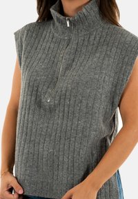 Top sin mangas de punto gris acanalado con cuello alto y detalle de cremallera corta en el cuello, que presenta una textura suave y un corte relajado.