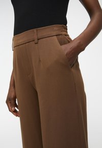 Pantalons larges marron en tissu texturé, avec une taille cintrée, des poches latérales et une silhouette lisse.