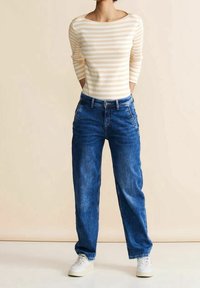 Randig beige och vit långärmad tröja i kombination med blå denimjeans. Jeansarna har en avslappnad passform och bärs med vita sneakers.