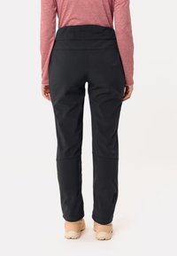 Zwarte buitenbroeken met een hoge taille, met een gladde textuur en subtiele naden, gecombineerd met lichtgekleurde schoenen.