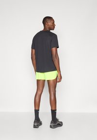 Completo sportivo da uomo composto da una maglietta nera a maniche corte, pantaloni corti verde neon, calze nere e scarpe da ginnastica grigie.
