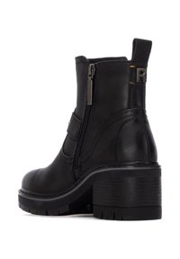 Stivale alla caviglia in pelle nera con tacco spesso, zip laterale e cuciture decorative. Presenta una linguetta con il logo "R" sul retro.