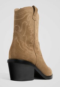 Jasnobrązowy zamszowy but za kostkę ze kwadratowym noskiem, blokowym obcasem oraz kontrastowym zdobieniem w postaci misternych wzorów zachodnich.