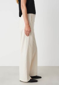 Beige wijde broek met een gladde afwerking. Voorzien van vo pockets en een hoge taille. Gecombineerd met zwarte puntige flats en een zwart top.