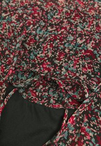 Robe florale avec un fond noir, ornée de petits motifs rouges, teal et crème, et d'un détail de nœud noué au niveau du cou. Tissu léger.