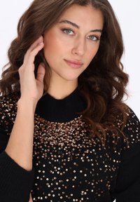 Zwarte trui met een hoge halslijn, voorzien van een spreiding van gouden pailletjes op het bovenste deel, wat zorgt voor een textuur en een versierde uitstraling.