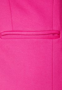 Tissu rose vif présentant une texture lisse avec un design de poche plate, soigneusement intégré dans la couture du vêtement.