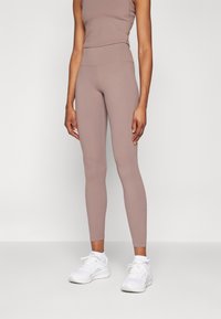 Leggings de color marrón claro con una cintura alta, hechos de tejido elástico, combinados con una camiseta sin mangas a juego y zapatillas deportivas blancas.