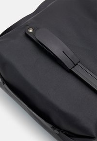Borsa in tessuto nero con una superficie liscia, dotata di una chiusura nera opaca e di un sottile dettaglio delle cuciture. Design semplice e funzionale.