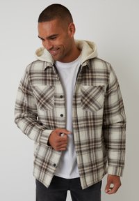 Kurtka w kratę w kremowych, brązowych i czarnych odcieniach, z miękkim, futrzanym kapturem. Posiada dwie przednie kieszenie i zapinanie na guziki.