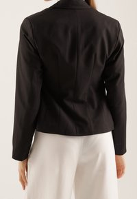 Black fitted blazer with a structured design, featuring a notched collar and long sleeves. Smooth fabric with tailored seams.