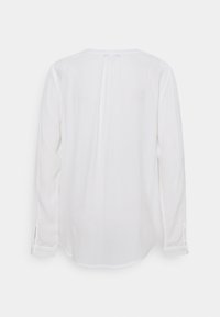 Biała bluzka z długim rękawem o okrągłym dekolcie, miękkiej fakturze i detalach w postaci plisy na plecach. Zapięcie na guziki przy mankietach oraz lekko zwężany dół.