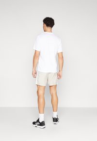 T-shirt blanc à manches courtes, short beige clair avec des rayures sur les côtés, chaussures de sport noires avec des accents blancs, vu de dos.