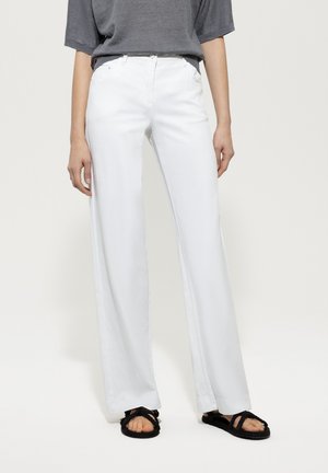 White wide-leg jeans with a smooth texture, featuring front pockets and a button closure, paired with black flat sandals.