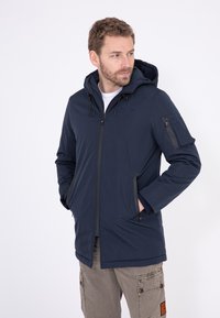 Dunkelblaue Kapuzenjacke aus weichem Material, mit einem Frontreißverschluss, seitlichen Taschen und einem strukturierten Patch am Arm.