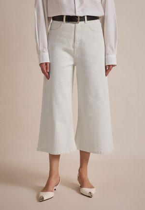 White wide-leg denim culottes with a high waist, featuring belt loops and a raw hem. Paired with white pointed-toe slingback shoes.