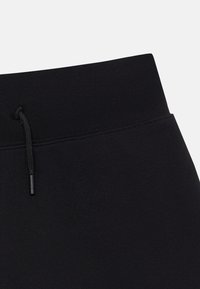 Ceinture de jogging noire avec une finition lisse, dotée d'un cordon de serrage avec une extrémité en plastique noir. Le matériau semble doux et extensible.