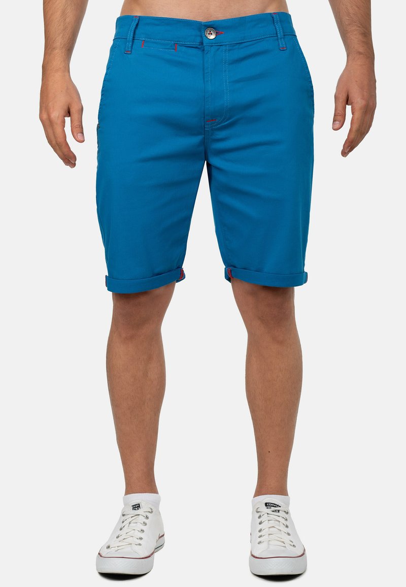 Blauwe katoenen shorts met omgeslagen mouwen, contrasterende rode stiksels en knoopsluiting. Bevat zij- en achterzakken voor opslag.