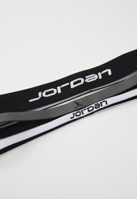 Kolme urheilupäähinettä mustana, harmaana ja valkoisena. Jokaisessa pannassa on "Jordan"-logo kontrastavilla väreillä ja teksturoidulla kankaalla.
