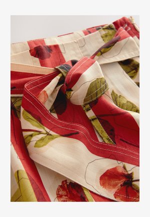 Textilný výrobok s kvetinovým vzorom v červenej, krémovej a zelenej farbe s detailom uviazanej mašle. Ľahký materiál s viditeľnými švami.