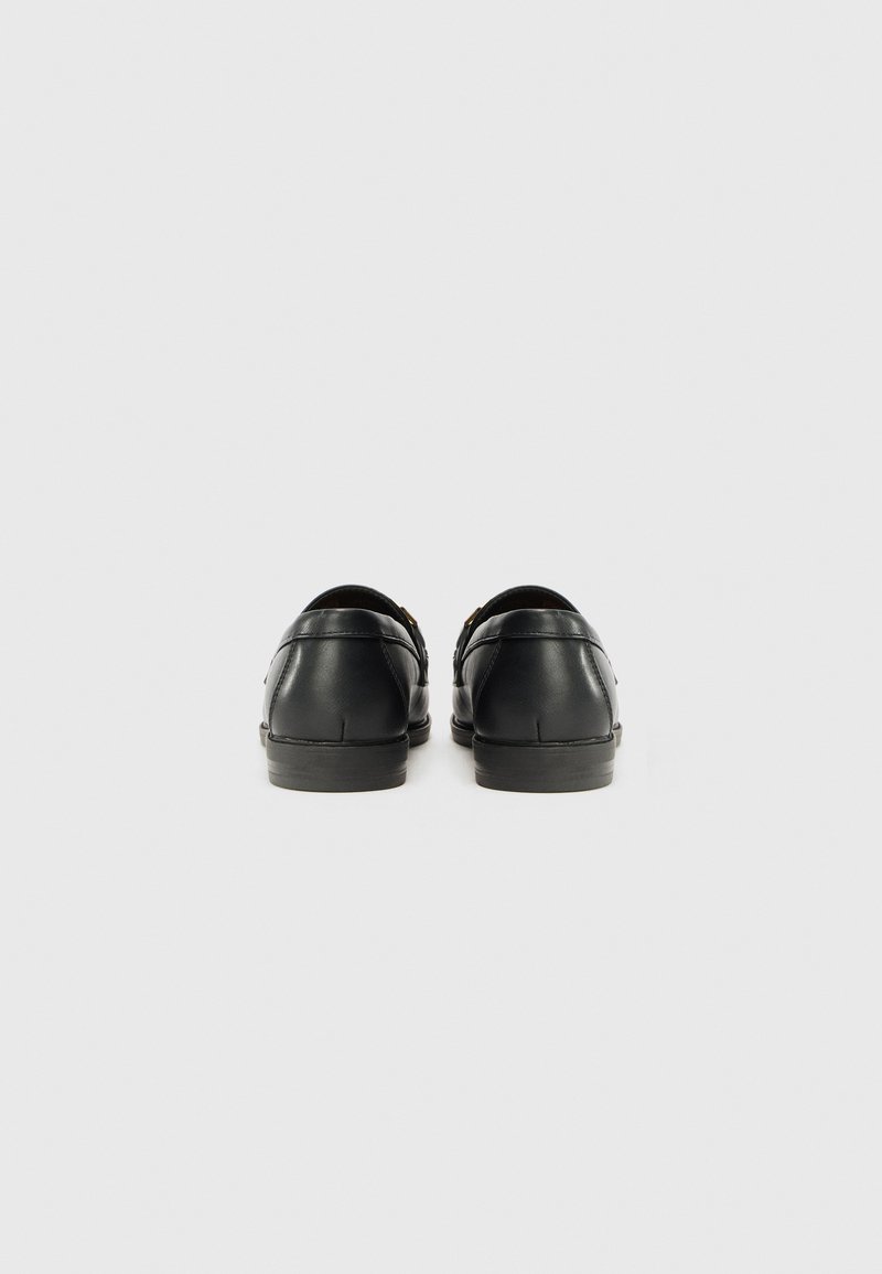 Zapatos de cuero negro con una textura suave y puntera redondeada. La vista trasera muestra un tacón bajo y un diseño minimalista. Sin hardware ni patrones visibles.