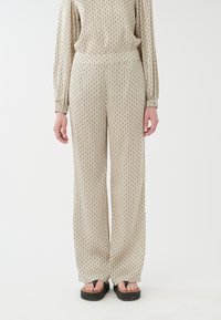 Pantalons amples en beige avec un motif géométrique noir. Fabriqués en tissu doux, avec une taille élastique et des poches latérales.