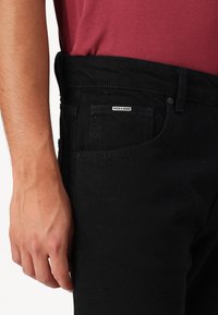 Juodos denim kelnės su liekna forma, turinčios penkių kišenių dizainą, subtilią tekstūrą ir mažą "Pegador" etiketę ant diržo.