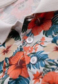 Blommig polo tröja med livfulla mönster av orange och blå blommor, vita knappar och ett texturerat tyg med en stickad krage.