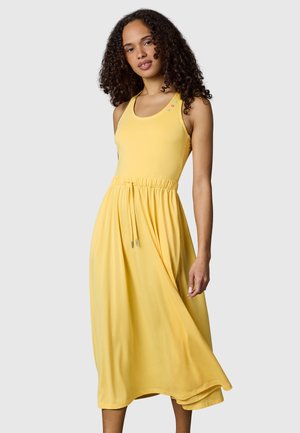 Frau mit lockigem Haar trägt ein ärmelloses gelbes Midikleid mit Tunnelzug in der Taille und bunten Knöpfen in der Nähe des Ausschnitts.