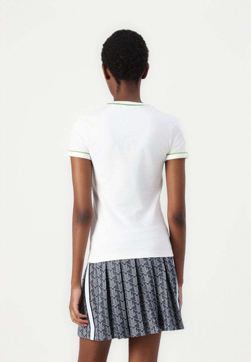 Biała koszula z krótkim rękawem z zielonym wykończeniem, w połączeniu z plisowaną spódnicą z geometrycznym wzorem w granatowo-białe pasy, prezentującą warstwowe faktury.