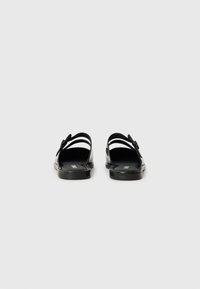 Black sandals with a smooth, glossy finish, featuring two wide straps, a contoured footbed, and a flat sole. Minimalist design without embellishments.