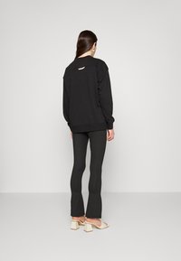 Black sweatshirt with a wide neckline and back cutout, paired with black flared leggings. Model wears beige block-heeled sandals.