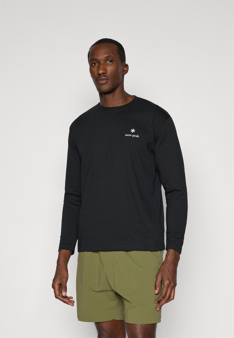 Black long-sleeve shirt with a round neckline, featuring a white logo on the chest, paired with olive green shorts in a lightweight fabric.