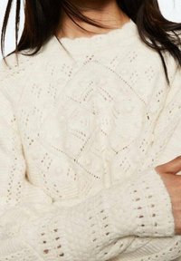 Pull en tricot crème avec un motif texturé en forme de losanges et des détails ajourés, encolure en forme d'ondulations et poignets côtelés.
