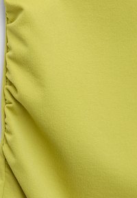 Tissu jaune clair à la texture lisse, présentant des fronces sur un côté, offrant une apparence douce et extensible.