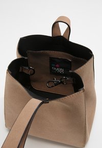 Ruskea teksturoitu mokkalaukku, jossa musta sisusta, yläaukaisu ja irrotettava lukko. Ominaisuuksiin kuuluu kontrastisaumaus ja logotunniste.