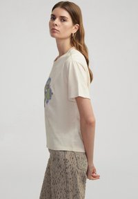 Camiseta de manga corta beige de algodón con un diseño abstracto colorido en el frente, combinada con una falda marrón claro que presenta un patrón de manchas.