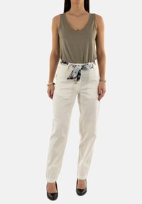 Pantalon blanc avec une ceinture à imprimé serpent, associé à un haut sans manches de couleur vert olive. Le tissu semble lisse avec un léger éclat.