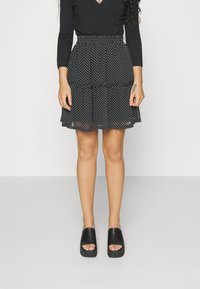 Černá sukně s puntíky, s rozšířeným, vrstveným designem a elastickým pasem, doplněná otevřenými černými platformovými botami.