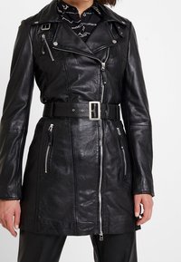 Svart lädermotorcykeljacka med en figurnära design, silverfärgade dragkedjor, bälte i midjan och långa ärmar. Har dragkedjefickor och slagkrage.