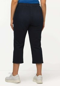 Pantalones cropped de mezclilla oscura con cintura alta, que presentan una textura suave y puños rematados, combinados con zapatillas deportivas blancas.