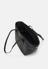 Svart läderhandväska med texturerad yta, öppen design och inre fickor. Har långa remmar och en diskret logotyp på framsidan.